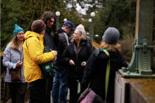 A group of people examining lichens together on a bridge in a wooded park.