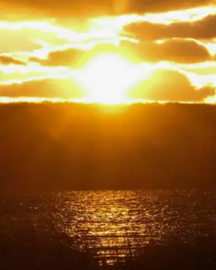 Sunset over water with the headline “Should We Make Daylight Saving Time Permanent?”