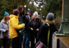 A group of people examining lichens together on a bridge in a wooded park.