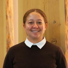 A profile photo of Andrea Durant, who is wearing a brown sweater and standing in front of wood panels.